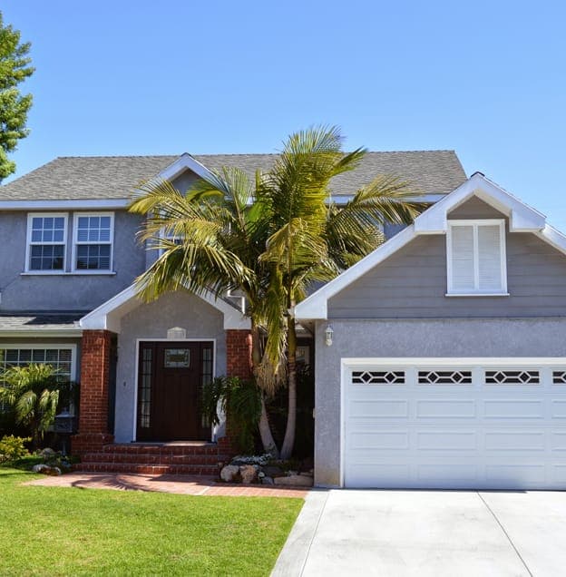 Grey and white colored new custom home exterior with a front lawn and garage, and a clear blue sky above.