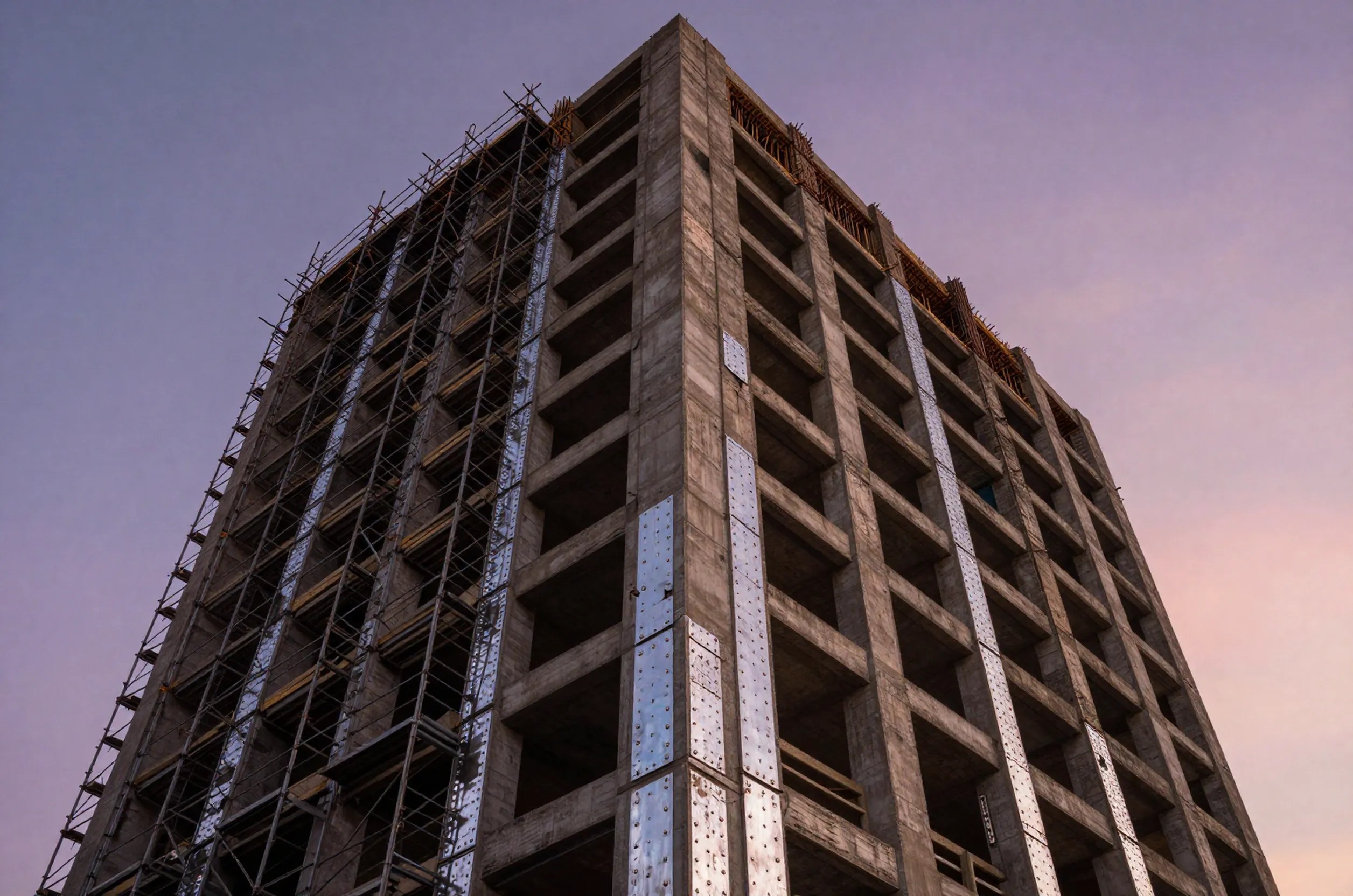 Low-angle view of an eight-story vintage apartment in West Hollywood with scaffolding and seismic retrofit plates at dusk.