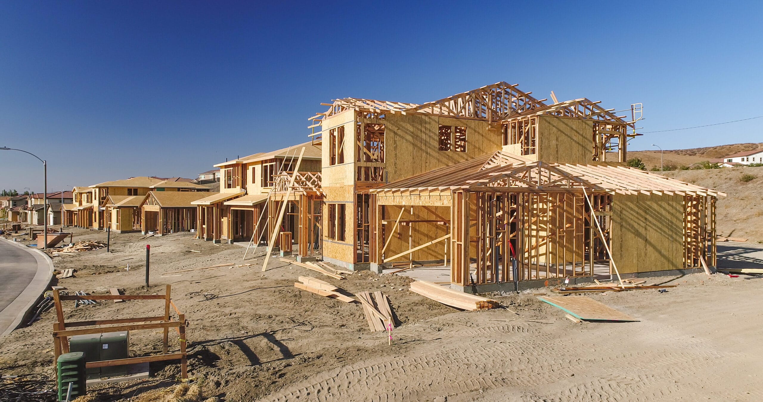 A row of houses under construction in a suburban area, showcasing wooden framing and early structural development, illustrating the rebuilding process after wildfire damage
