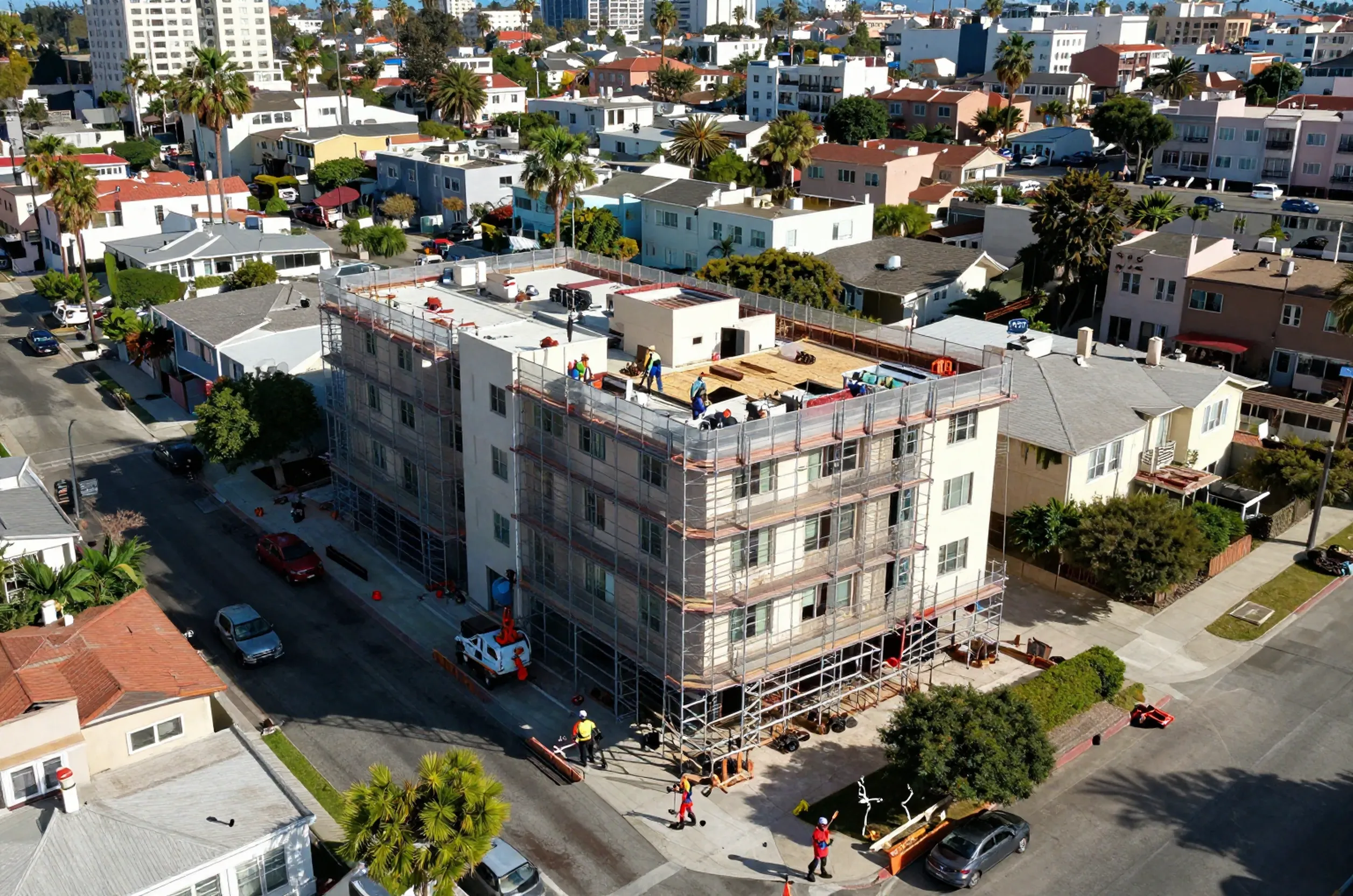 Aerial view of a West Hollywood neighborhood showing a seismic retrofit on a soft-story building, with workers and cranes.