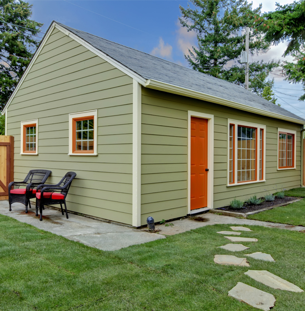 Olive green-colored single-story backyard ADU with grey roof and reddish-brown doors and windows.